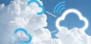 Um céu azul durante o dia com várias nuvens, dentre as nuvens surgem desenhos representando as nuvens relacionadas a tecnologia. São três desenhos, uma nuvem branca e duas azuis interligadas por pontinhos brancos.